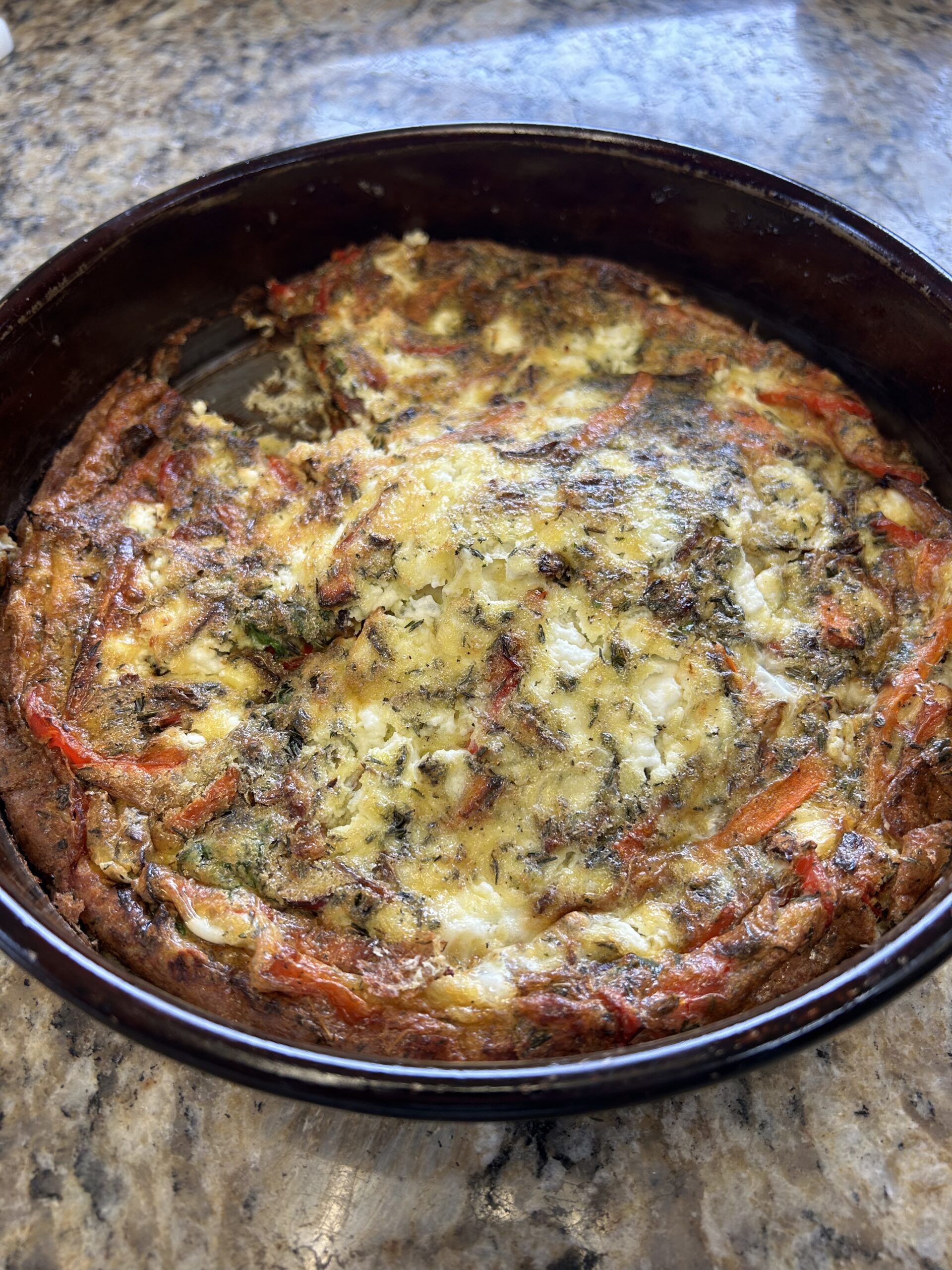 Herbed goat cheese egg bake with roasted carrots, peppers, onions, and fresh parsley in a round baking dish.